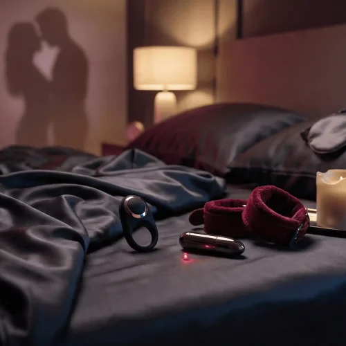 Mejores regalos sexuales para parejas con juguetes eróticos elegantes sobre una cama y sombras de pareja al fondo.